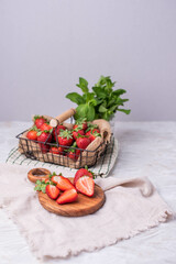 Strawberries in a wire basket on a table with a wooden board and sliced strawberries and fresh mint in a jar