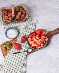 Schale mit geschnittenen Erdbeeren auf einem Brett und einer kleinen Schale Zucker, Korb mit...