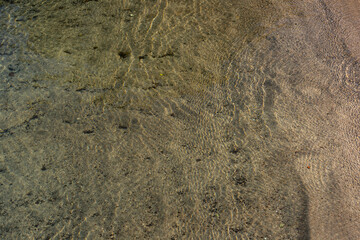 Sun shining through shallow water on a sand beach.