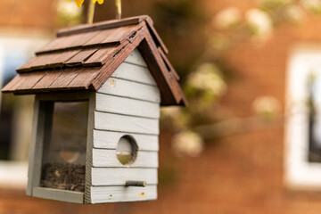 Bird feeder in shape of a little house with glass on sides to see birds eating from it. Birdhouse made out of wood in white and brown, bird house for small songbirds only.