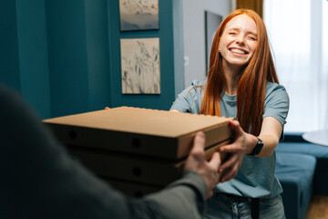 Happy excited young woman receiving carton boxes with pizza from unrecognizable courier male on doorway at home. Back view of delivery man delivering boxes with food to female client at apartment. - obrazy, fototapety, plakaty