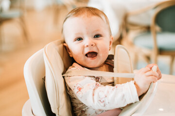 Small baby girl sitting in a high chair eating and smiling