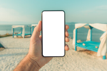 Mobile smart phone with blank mockup template screen in male hand, beach pergola in background