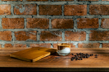 A Glass of Dirty coffee by espresso shot topped over cold fresh milk create a gradient layer in the morning over a red bricks wall background and coffee beans on a wooden Cafe table. For Copy Space