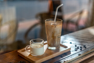 A tall glass of iced latte coffee with milk cream on a wooden counter bar over a cafe glass window reflex at a Cafe coffee shop. Cold brew refreshment summer drink with copy space Selective focus