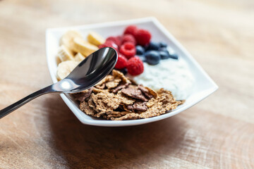 Yogurt bowl with fresh berries, granola and banana served on living room table at home.