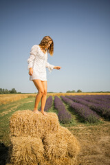 Naklejka na ściany i meble Happy pretty blonde girl in a white dress on a golden hay in the field, summer vacation