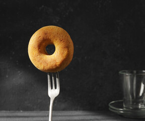 Alone Donut on the fork in the sun rays on the dark background , copy space