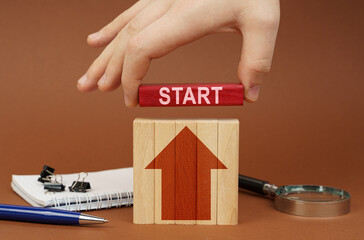 On a brown surface are office items, wooden blocks, in the hand is a red block with the inscription...