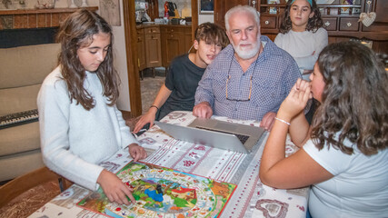 Fototapeta premium Grandfather using laptop indoor with his grandchildren.