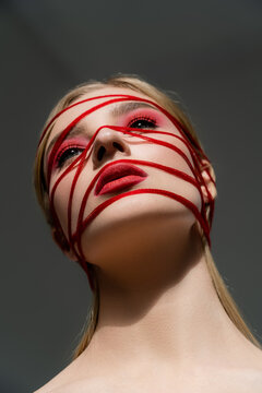 Low angle view of woman with red makeup and threads isolated on grey.