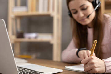 Girl listen headphones and writing on notepad. Student woman online larning