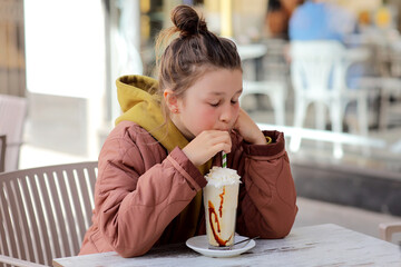 Adorable cute preschooler caucasian girl portrait drinking fresh tasty vanilla milkshake cocktail at cafe outdoors. Children healthy diet and nutrtion concept. High quality photo