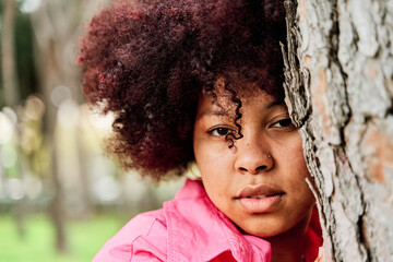 Portrait of a curly-haired African-American woman leaning against a tree.