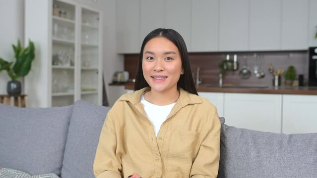 Attentive participant of virtual meeting, webinar. Intelligent Asian woman student waving at camera, greeting participants of video conference, listening speacker carefully and nodding, webcam view