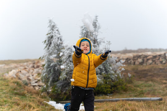 A happy child is throwing snow against the backdrop of small Christmas trees