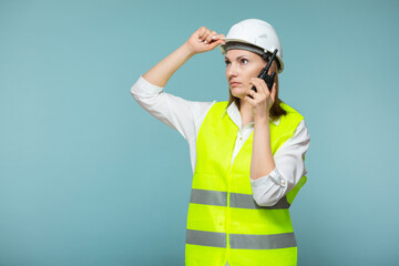 Professional engineer. A woman in a protective helmet and a bright vest gives instructions on a walkie-talkie, on a blue background. Copy paste.