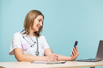 A woman doctor sits at a table and carries out an online consultation by phone, on a blue background. Copy paste. healthcare concept.