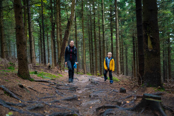 Mum and her little son go on a mountain trail in wet autumn weather.