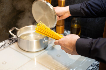 Close-up. A man cooks spaghetti in the kitchen. He dips the pasta into a pot of boiling water.