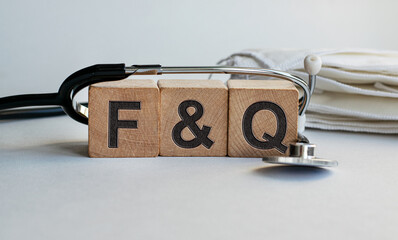 F&Q inscription on wooden cubes isolated on white background, medicine concept. A stethoscope and protective masks are on the table next to it.