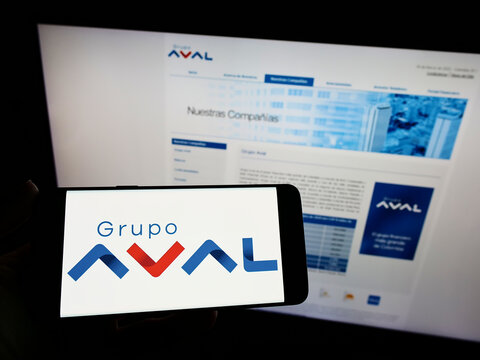 Stuttgart, Germany - 03-30-2022: Person holding smartphone with logo of Colombian Grupo Aval Acciones y Valores S.A. on screen in front of website. Focus on phone display.