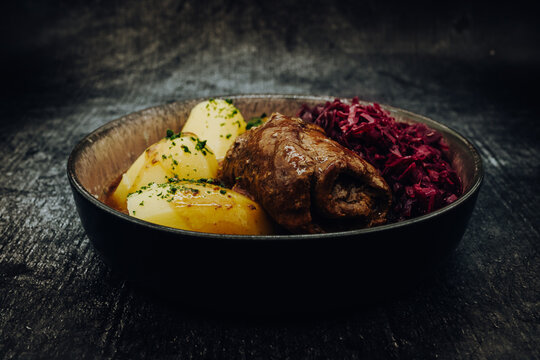 Leckere hausgemachte Rinderroulade mit Kartoffeln und Rotkohl in einer Schale und vor dunklem Hintergrund