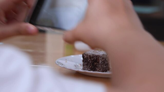 A young man takes a close-up photo on a phone with a macro lens of a cake with coconut strodna on a white plate