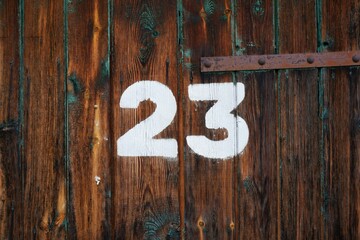 White colour number twenty three on an old abandoned weathered painted natural rusty brown wooden gate of a garage in Budapest suburb, Hungary