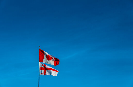 Mikmaq State flag flying on a pole with Canadian flag against blue sky background