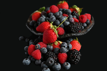 Assorted fresh berries in a bowl on black background