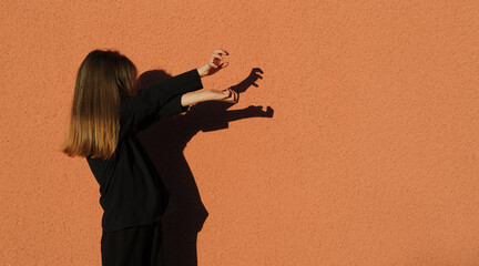 Girl playing, makes shadow theater on orange background