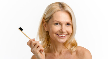 Toothbrush in hand of smiling mid age woman. Happy blonde 40s woman with naked shoulders and great...