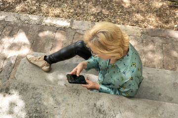 Blonde mature woman chatting while sitting in a bench in a park