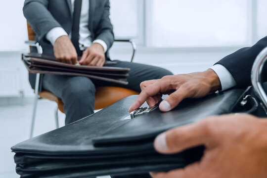 Man in a classic suit holds a brown briefcase close-up