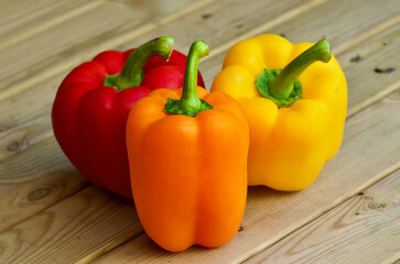 Closeup of three sweet peppers in different colors laying on a wooden table outdoors in summer.