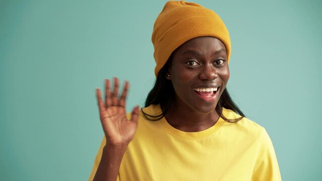 Cheerful African woman greeting at the camera in the turquoise studio