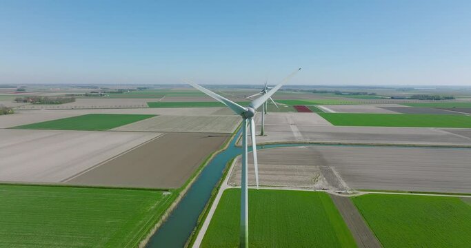 Wind turbines spin in a flat Dutch landscape on a clear day, Aerial view.