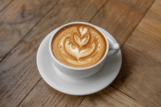 Hot coffee cup with milk late art foam on wood background