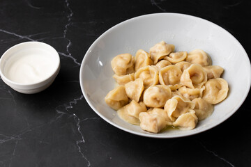 Meat dumplings, homemade russian pelmeni in bowl with sour cream isolated on black background