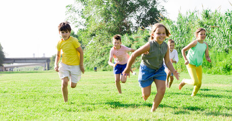 Fototapeta premium Group of school children, boys and girls, laughing and running in a city park at summer day