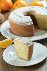 Close up piece of moist orange fruit cake on plate with orange slices on wooden table. Delicious breakfast, traditional English tea time. Orange cake recipe.