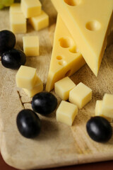 Cheese cut with fruits.Mazdar cheese, gouda cheese cubes and black grapes.Cheese with grapes berries on wooden board background.milk fat and Milk products.