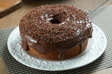 Brazilian carrot cake with chocolate frosting on wooden table with carrots in the background
