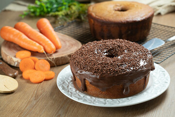 Brazilian carrot cake with chocolate frosting on wooden table with carrots in the background