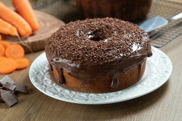 Brazilian carrot cake with chocolate frosting on wooden table with carrots in the background