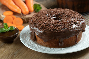 Fototapeta na wymiar Brazilian carrot cake with chocolate frosting on wooden table with carrots in the background
