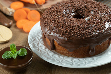 Brazilian carrot cake with chocolate frosting on wooden table with carrots in the background