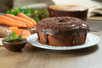 Brazilian carrot cake with chocolate frosting on wooden table with carrots in the background