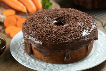 Brazilian carrot cake with chocolate frosting on wooden table with carrots in the background